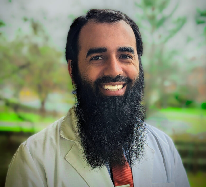 Headshot of Doctor Mohammad Khubaib, MD, CAQSM from the shoulders up smiling in front of a nature background.